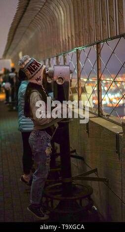 A teenage girl looking through coin-operated binoculars from atop the Empire State Building in New York City. Stock Photo