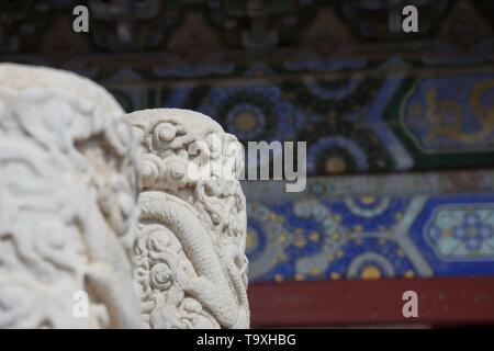 Detail at a Chinese temple - intricately carved white marble pillar in focus; blue complex painted wall in background Stock Photo