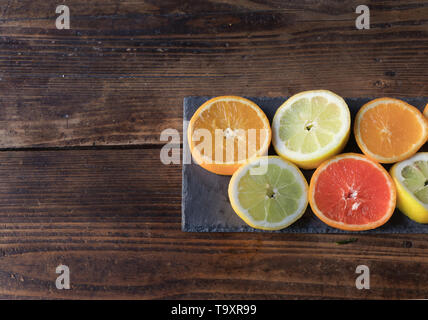 Sliced lemons and oranges cut on a slate board, on a wooden table Stock Photo