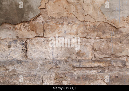 Old ruined wall facade with fallen cement and bricks. Texture background flake off plaster from house wall. Stock Photo