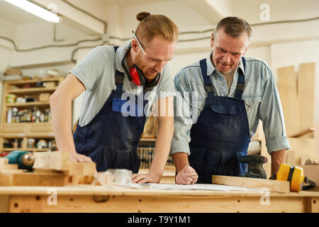 Waist up  portrait of senior carpenter teaching apprentice  while working together  in joinery workshop Stock Photo