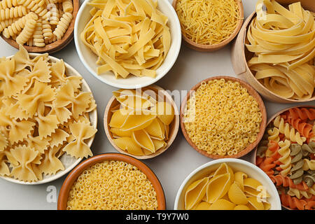 Bowls with assortment of uncooked pasta on grey background Stock Photo