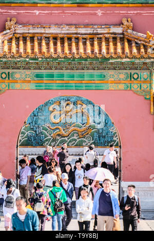 Tourists pass a gate in Forbidden City in Beijing China with a dragon in the back ground Stock Photo