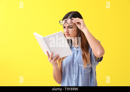 Woman with bad sight trying to read book on color background Stock Photo