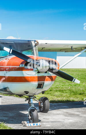 Front view of old red and white single engine propeller plane on grass field in sunshine. Stock Photo