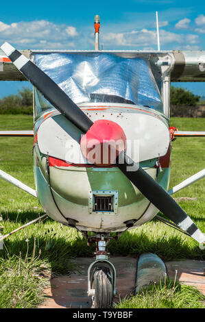 Old red and white single engine propeller airplane, front view, parked on grass field on sunny day. Stock Photo