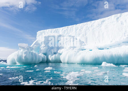 Snowy white iceberg floating in aquamarine blue or turquoise water of the Southern Atlantic Ocean in Antarctica with blue sky and thin clouds above. Stock Photo
