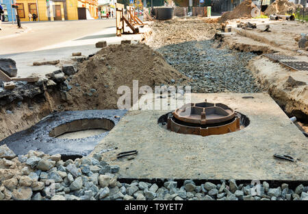 Concrete blocks, wells and pipes of the city collector lie near the excavated trench on the roadway of the street Stock Photo