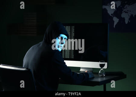 Professional hacker in mask using computer in dark room Stock Photo
