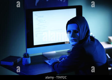 Professional hacker in mask using computer in dark room Stock Photo