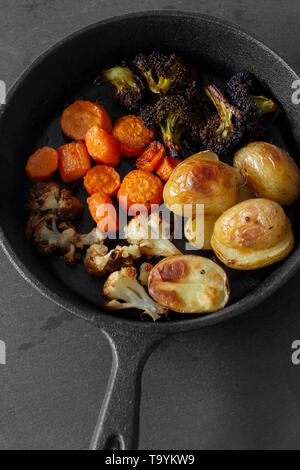 Roasted fried vegetables in a cast iron pan with potato, cauliflower, carrot and broccoli.  On a slate background. Stock Photo