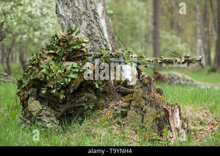 Camouflaged sniper in the forest in ambush. Military man aiming a gun, a rifle at the enemy in nature Stock Photo