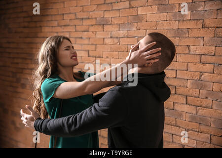 Young woman defending herself from attack by thief against brick wall Stock Photo