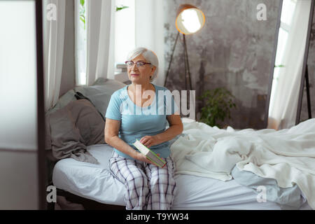Beautiful woman preparing to open book while sitting on bed. Stock Photo