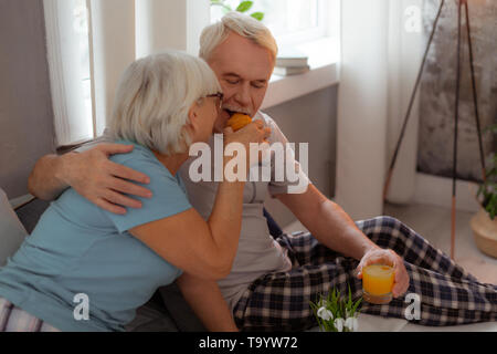 Nice-looking lady feeding up her husband with a freshly-baked croissant Stock Photo