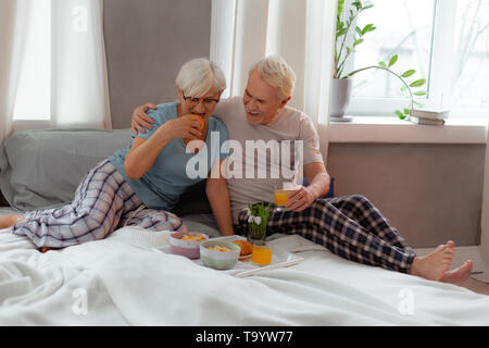 Nice-appealing wife eating croissant while her husband is cuddling her Stock Photo