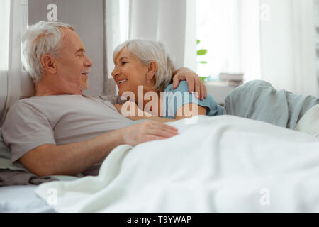 Beaming silver-haired bearded man embracing his smiling aged short-haired spouse Stock Photo