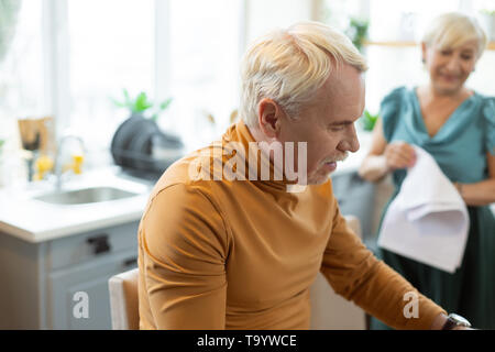 Stylish handsome attractive grey-haired bearded man sitting at the kitchen. Stock Photo