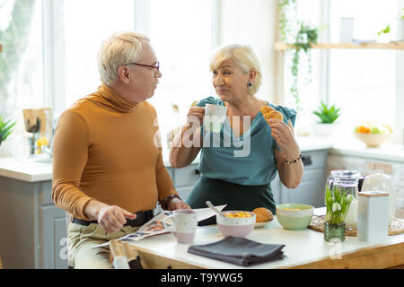 Cheerful couple having breakfast and chatting at the kitchen table Stock Photo