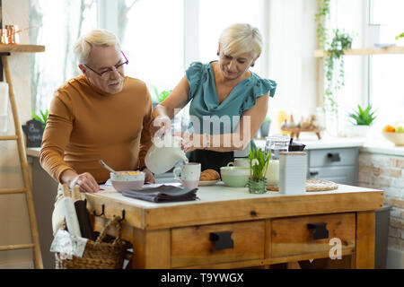 Kind elderly grey-haired female pouring tea into the cups Stock Photo