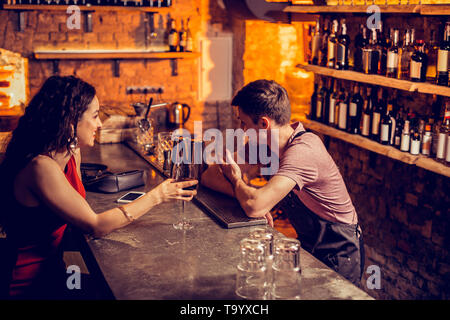 Dark-haired woman speaking with barman and drinking wine Stock Photo