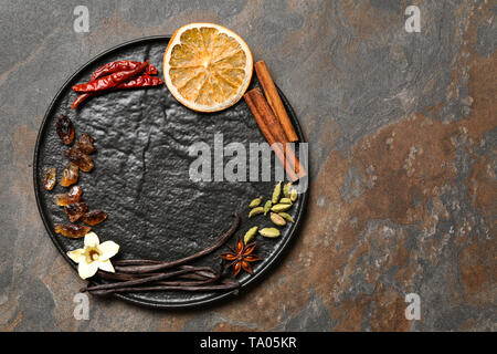 Plate with aromatic vanilla sticks and different spices on grunge background Stock Photo