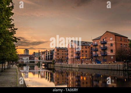 Brick apartment buildings and renovated warehouses along the river Aire in Leeds at Sunset. Reflection in water. Stock Photo