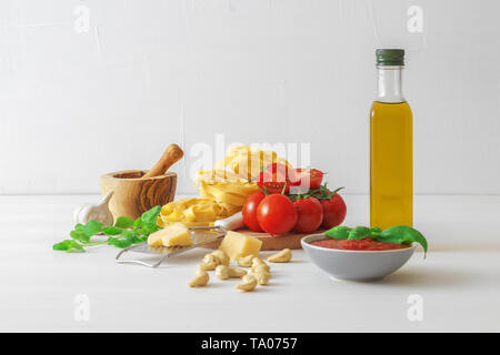 Table with ingredients to make tomato pesto. Tomatoes, garlic, fresh oregano and basil herbs, bottle of olive oil, few cashew nuts, parmesan cheese, c Stock Photo