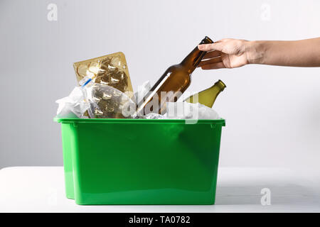 Woman putting empty glass bottle into trash bin on light table. Recycle concept Stock Photo
