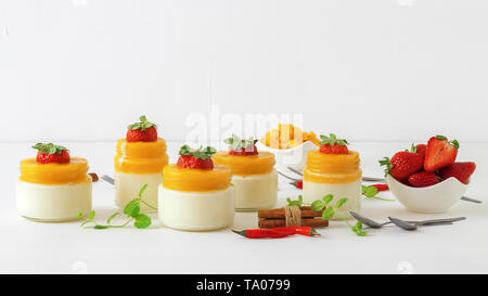 Traditional Italian sweet dessert Panna cotta with mango jelly with touch of red hot chili Piri-Piri served in jars on white wooden table and embellis