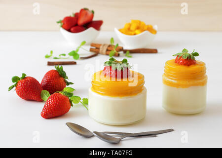 Traditional Italian sweet dessert Panna cotta with mango jelly with touch of red hot chili Piri-Piri served in jars on white wooden table and embellis Stock Photo