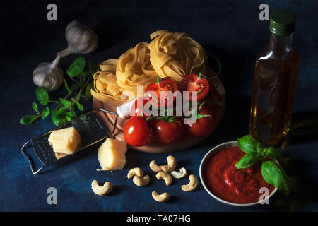 Table with ingredients to make tomato pesto. Tomatoes, garlic, fresh oregano and basil herbs, bottle of olive oil, few cashew nuts, parmesan cheese, c Stock Photo