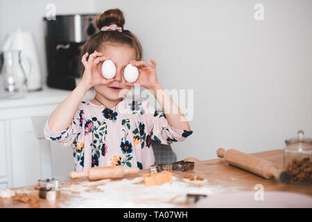 Smiling kid girl 4-5 year old having fun with raw eggs in kitchen. Making cookies indoors. Childhood. Stock Photo