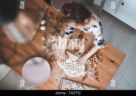 Little girl 5-6 year old playing with raw pastry and nuts on wooden table closeup. Childhood. Stock Photo