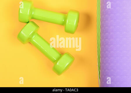 Shaping and fitness equipment. Barbells in small size on yoga mat, close up. Healthy shape and sport concept. Dumbbells made of light green plastic on yellow and purple background, top view Stock Photo