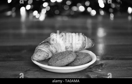 What do kids around world leave for Santa. Croissant and oat cookies on white plate. Winter holiday tradition. Sweets for Santa Claus and his helpers. Santa treats recipe. Treats for Santa concept. Stock Photo