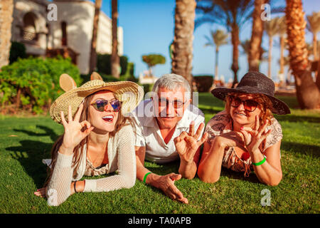 Senior couple lying on grass with adult daughter by hotel. Happy people enjoying summer vacation in Egypt. Family values Stock Photo