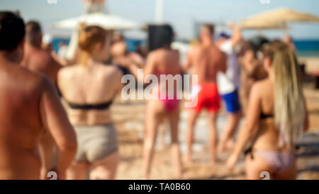 Defocused image of young people dancing on the sea beach at soap foam disco party. Stock Photo