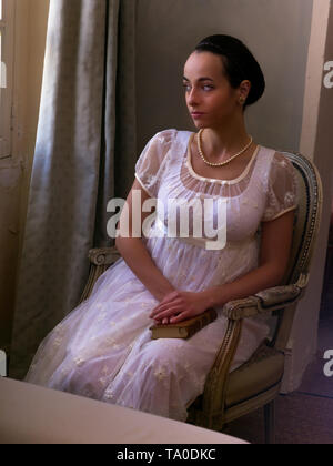 Young woman in authentic regency dress near a window of a classical interior Stock Photo