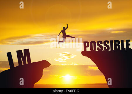 Man jumping over impossible or possible over cliff on sunset background Stock Photo