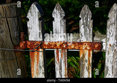 A white picket fence with a rusty red hinge Stock Photo