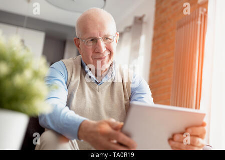 Elderly man using tablet PC. Senior sitting on sofa in living room Stock Photo
