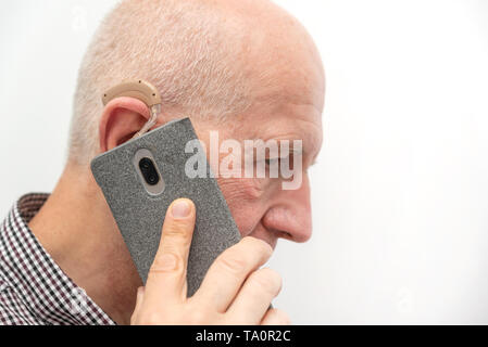 Hearing aid in the ear of aged old man. Senior using modern hearing aid while talking on the phone Stock Photo