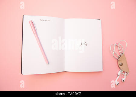 Opened diary with a pink pen and headphones on pastel millennial pink background. Concept of learning, blogging. Top view. Flat lay. Minimal style. Stock Photo