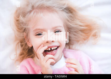 Laughing baby girl 4-5 year old lying in bed closeup. Looking at camera. Childhood. Positive emotions. Stock Photo