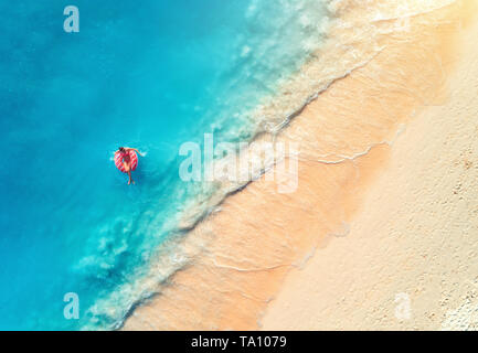 Aerial view of a young woman swimming with the donut swim ring in the clear blue sea with waves at sunset in summer. Tropical aerial landscape with gi