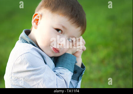 Cute boy is sitting on green grass. He is waiting. Concept of childrens happy Stock Photo