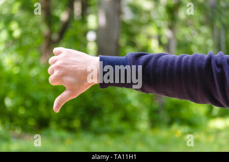 Thumb down hand sign. Gesture mens hand of dislike and negative. Concept of disagreement, disgust, unhappy. Closeup view on green nature background. M Stock Photo