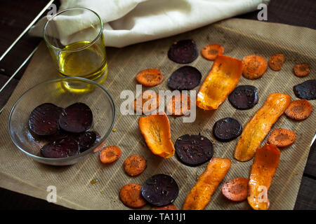 Preparing healthy beetroot and carrot chips with sea salt on baking paper.Thin slices of vegetables seasoned with spices and olive oil Stock Photo