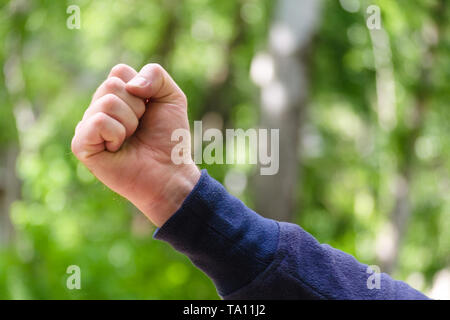 Clenched fist hand sign. Mens hand gesture of power and masculinity, success. Concept of brave, aggression, win. Close Up view on green nature backgro Stock Photo